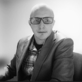 Caleb Hess, Creator of TechBitsBlog, sitting in a suit and glasses.